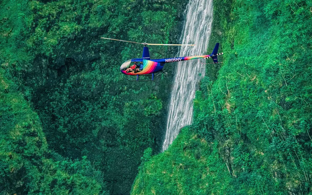 A helicopter beside a tall waterfall in the green Koolau cliffs of Oahu